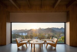 Una habitación moderna con un gran ventanal, dos sillones de mimbre y una mesa redonda.