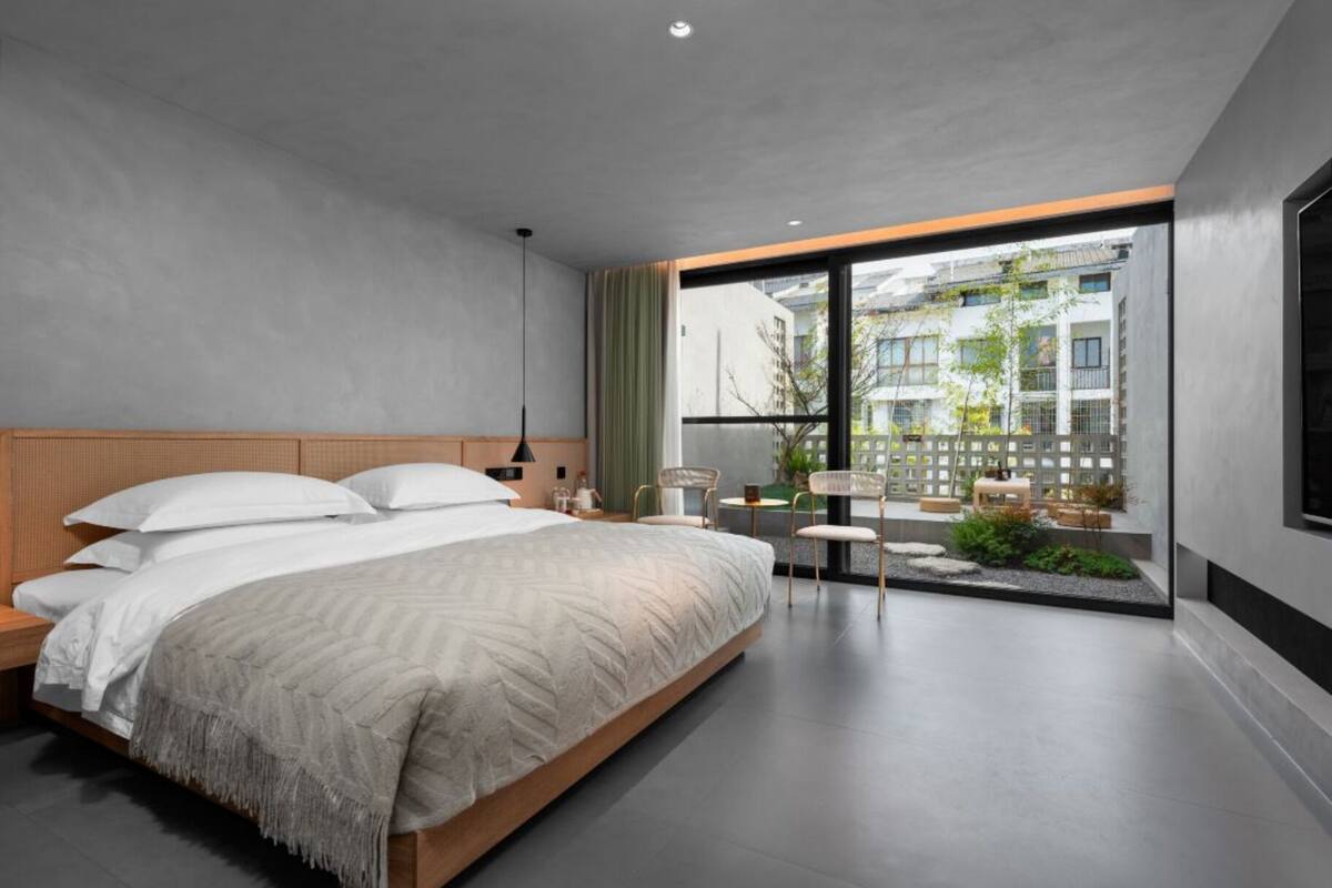 Une chambre moderne avec un grand lit, une petite table et des chaises, et une vue sur la ville grâce à de grandes fenêtres.