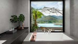 A modern bathroom with a large bathtub, a view of a mountain landscape, and a large window. - HUANG GUO SHU DUO BEI YUN SHE HOTEL (Anshun)