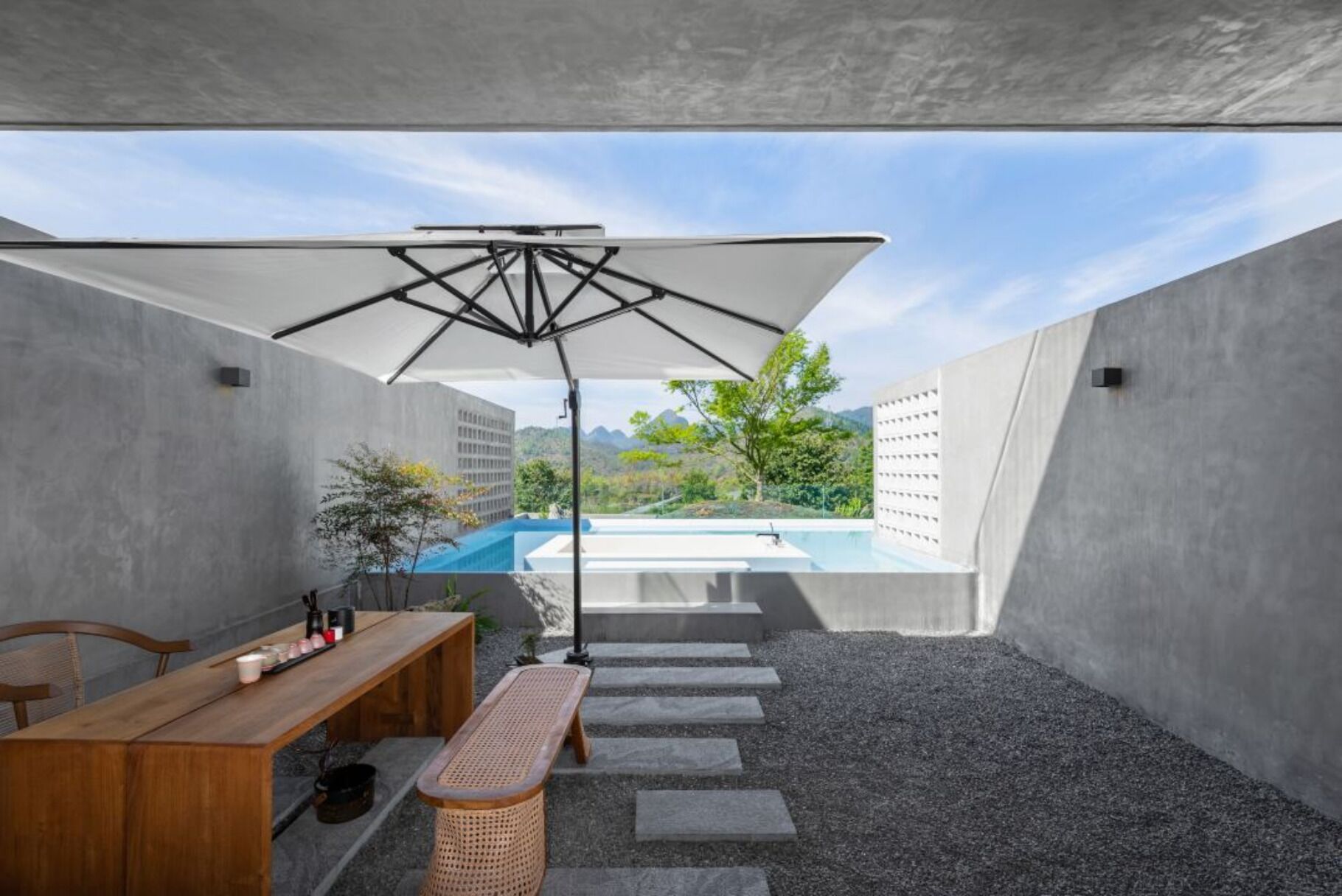 A modern outdoor space with a wooden bench, a table, and a large umbrella.