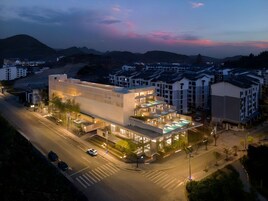 A modern hotel with multiple floors, a well-lit entrance, and a view of surrounding buildings and hills.