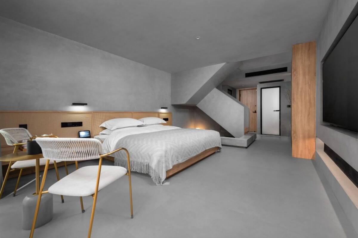 Une chambre moderne avec un grand lit, un bureau, deux chaises, une télévision et un escalier menant à un niveau supérieur.