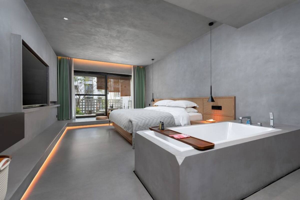 Une chambre d’hôtel moderne dotée d’un grand lit, d’une salle de bain séparée avec baignoire et d’un balcon avec rideaux.