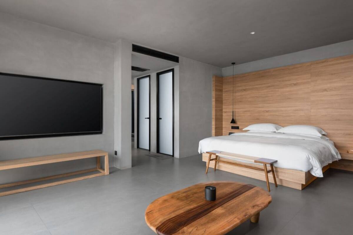 Une chambre moderne avec un grand lit, une tête de lit en bois, un banc et un téléviseur.