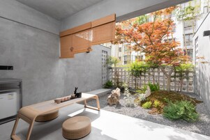 A modern interior with a concrete wall, a wooden table, and a view of an outdoor garden with trees and a fence.