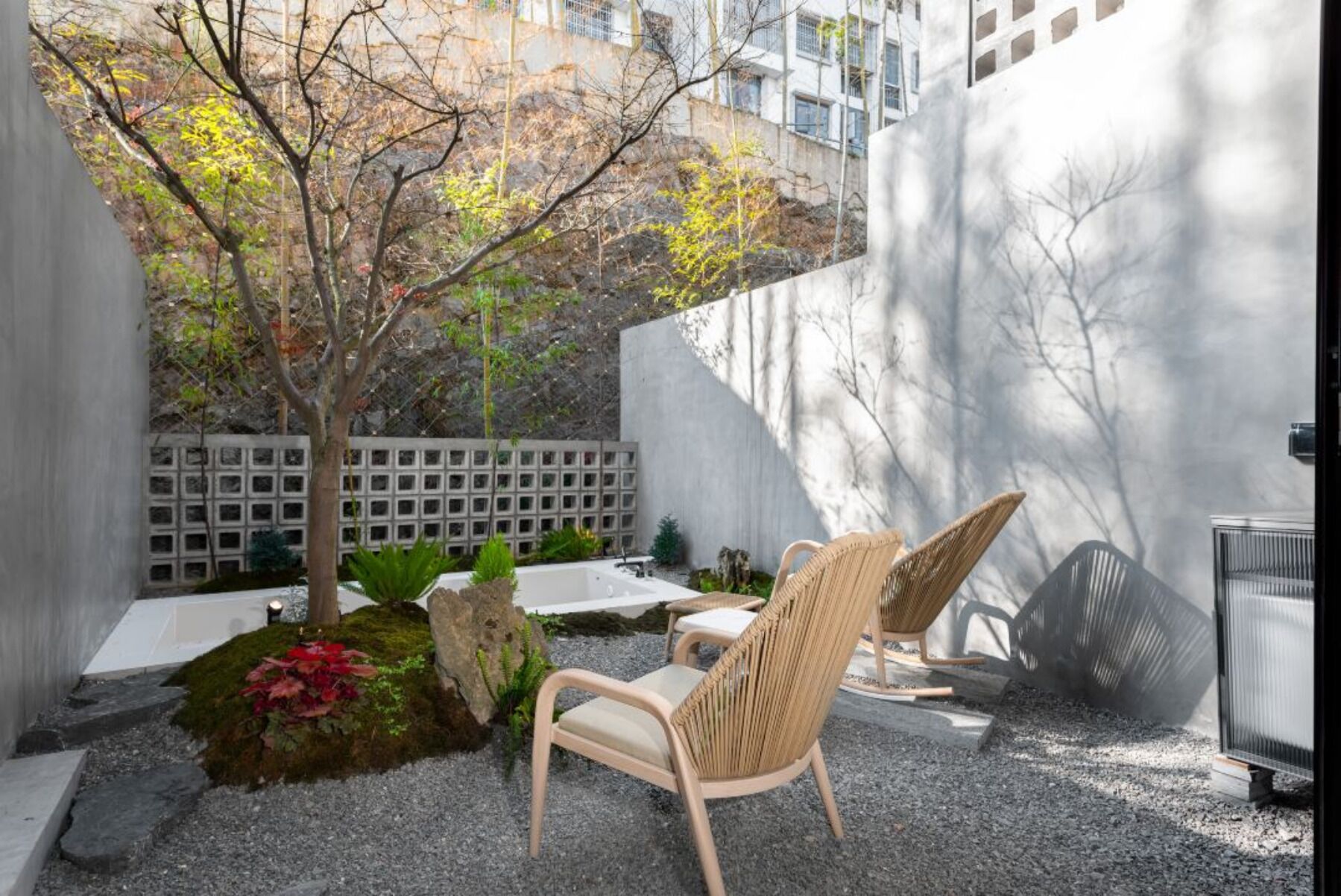 A modern outdoor seating area with two wicker chairs, a small table, and a decorative rock garden.