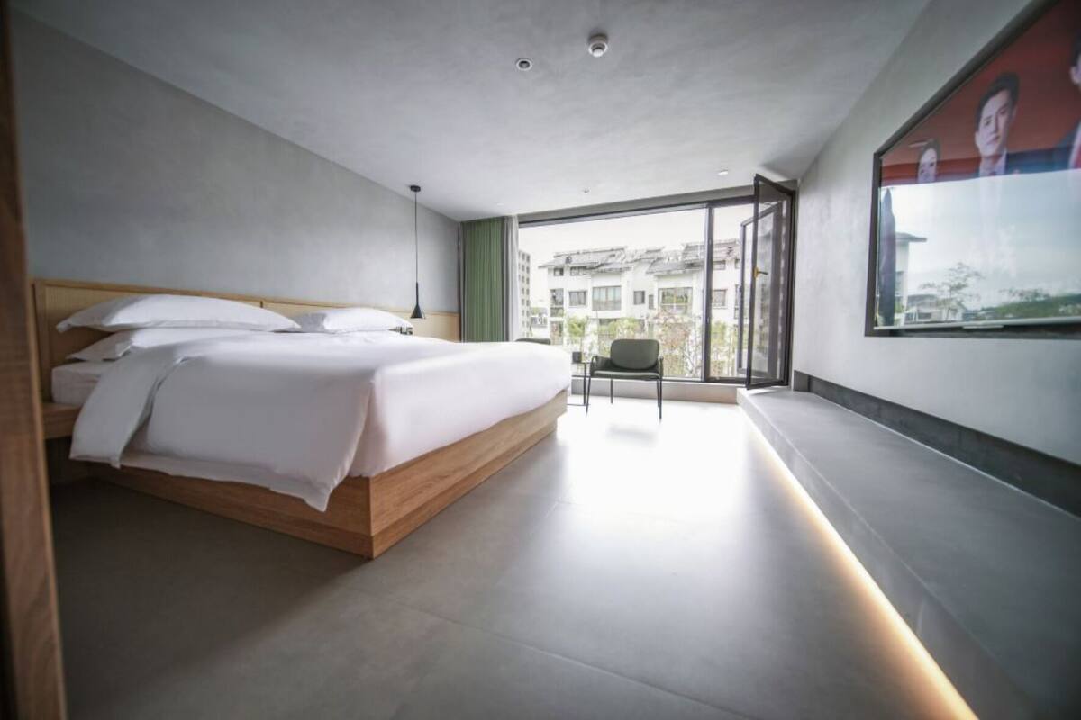 Une chambre moderne avec un grand lit, une chaise et une vue sur les immeubles à travers une grande fenêtre.