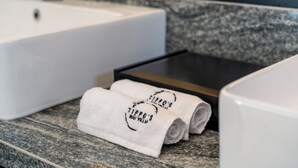 Un baño con un lavamanos blanco, encimera de granito y dos toallas enrolladas con un logotipo.