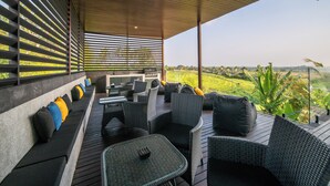 Un espacio de estar al aire libre cubierto con mobiliario de mimbre, una parrilla y vistas a un paisaje exuberante.