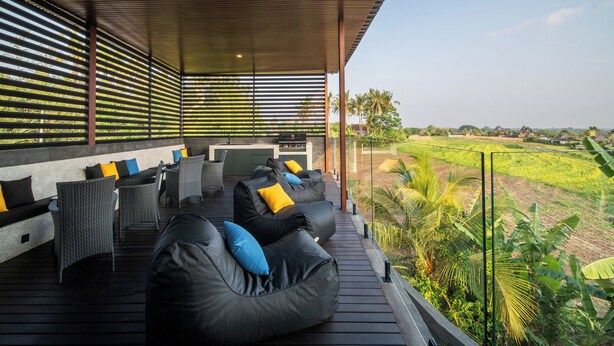 Un espacio al aire libre techado con sillones de mimbre y pufs de frijol negro, con vistas a un paisaje verde exuberante.