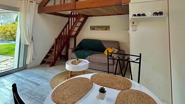 Un coin repas avec une table ronde, des sets de table en fibres tressées et un escalier menant à un niveau supérieur.