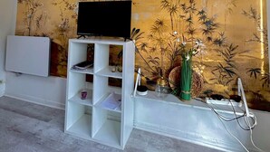 Une pièce dotée d’un téléviseur fixé au mur, d’une étagère blanche et d’un mur décoratif orné de motifs floraux et de bambous.