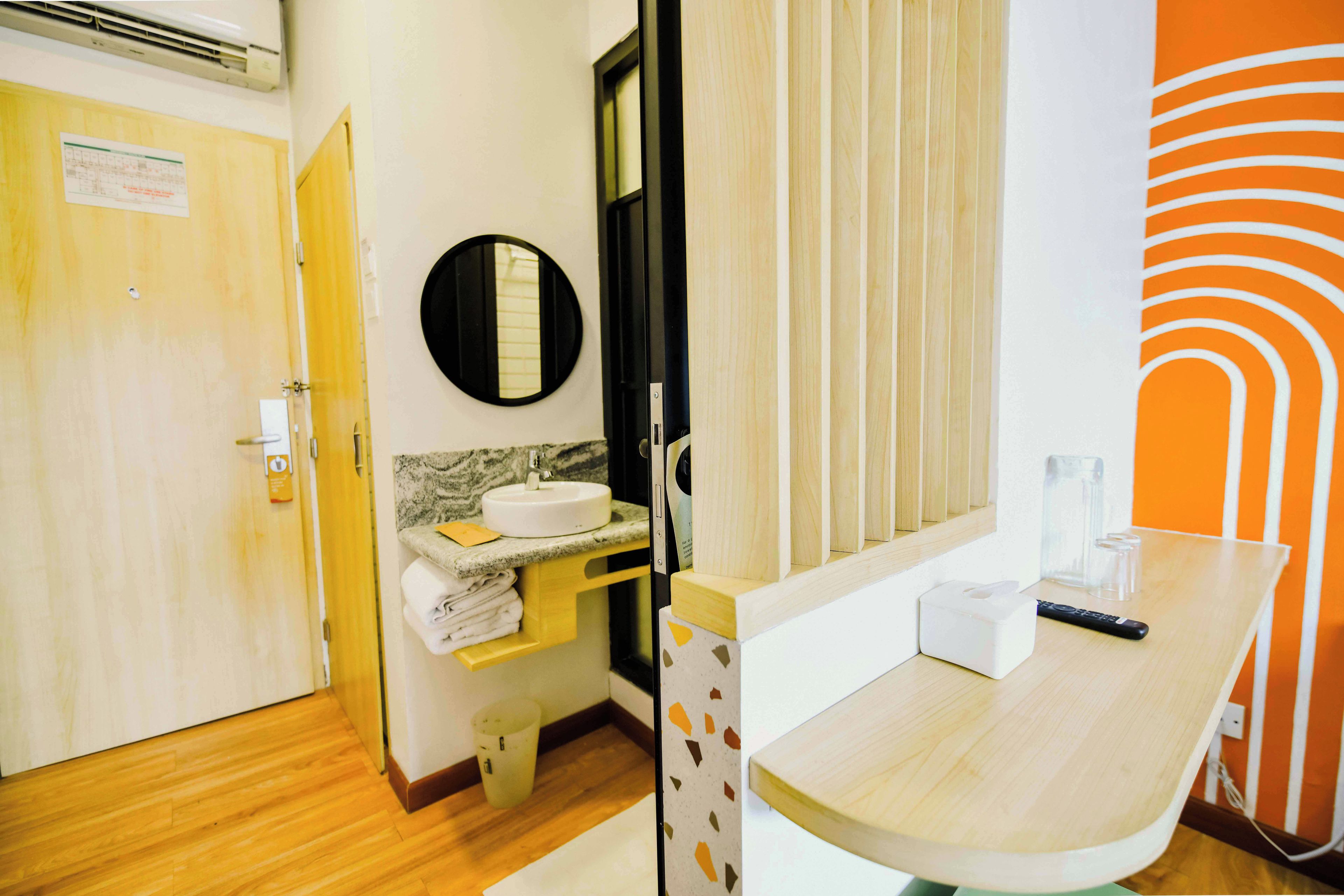 A hotel bathroom with a wooden floor, a sink with a mirror, a towel rack, and a toilet.