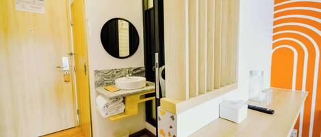 A hotel bathroom with a wooden floor, a sink with a mirror, a towel rack, and a toilet.