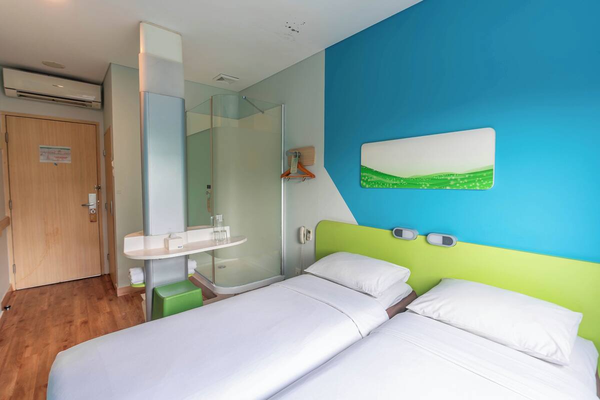 Een hotelkamer met twee bedden, een badkamer met een glazen douche en een schilderij aan de muur.