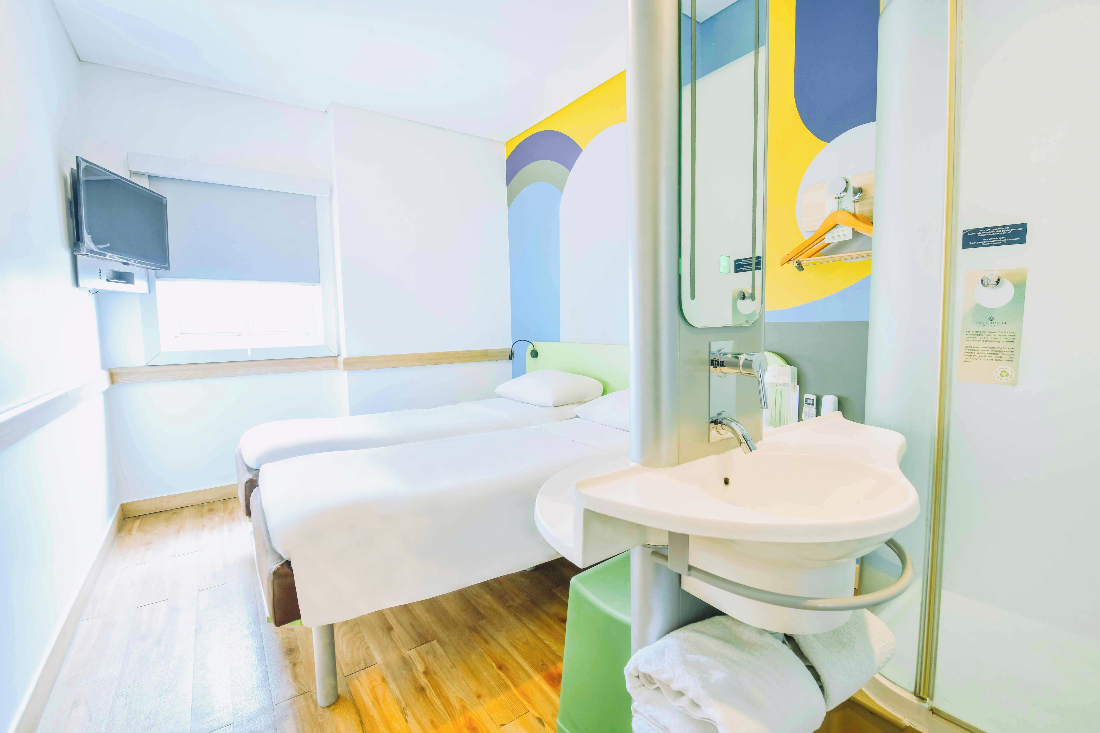 A hotel room with a bed, a bedside table, a mirror, a sink, and a window.