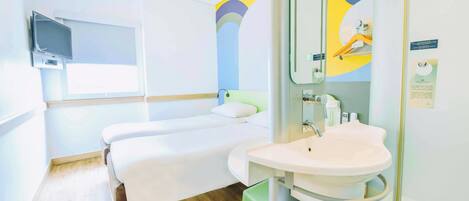 A hotel room with a bed, a bedside table, a mirror, a sink, and a window.