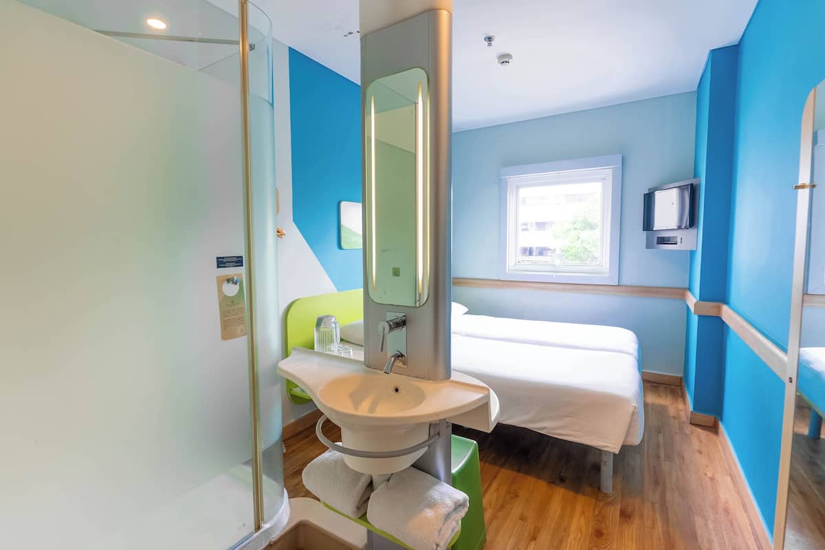 Een moderne badkamer met een douchecabine van glas, een wastafel met spiegel en een bed met een witte matras.
