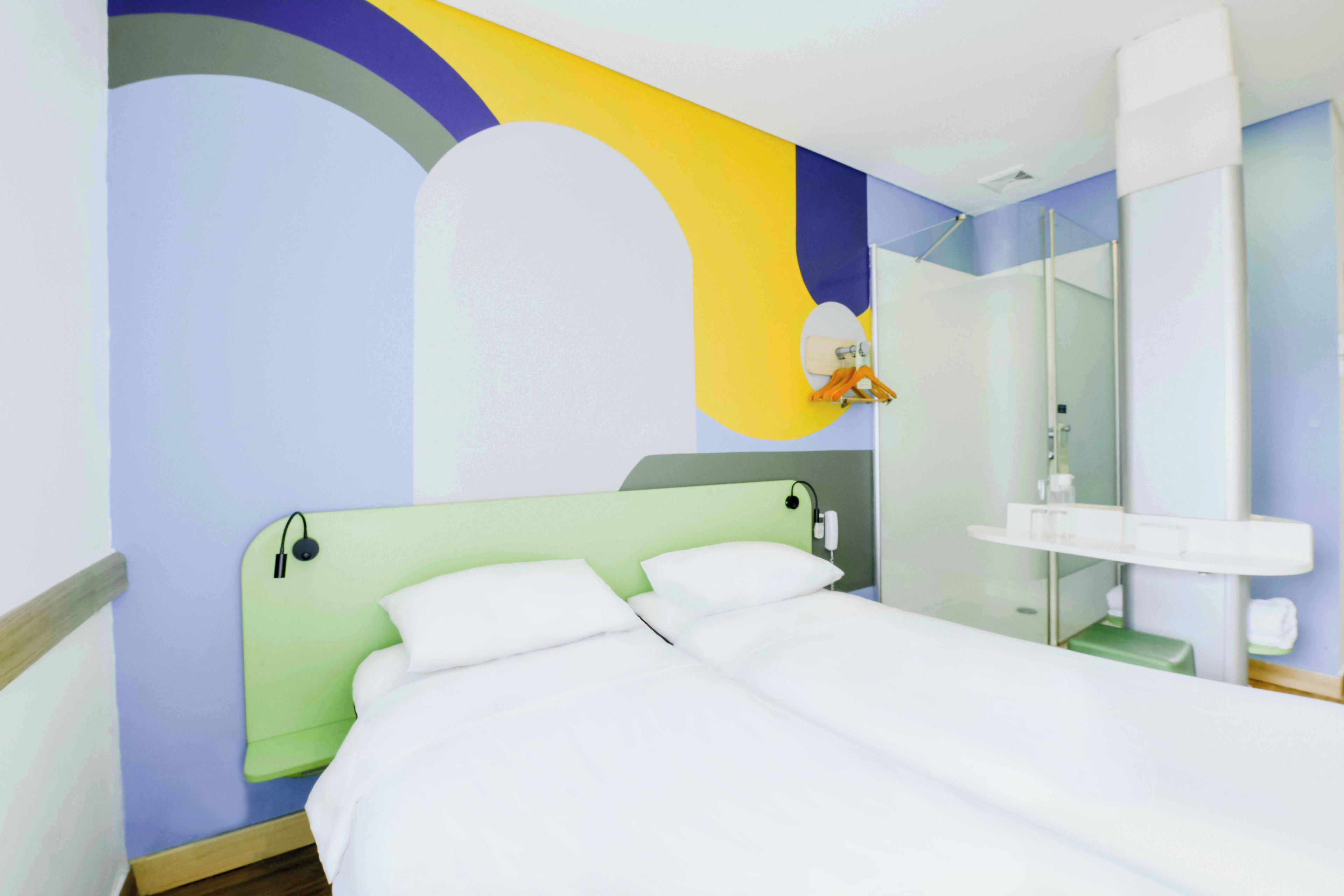 Habitación de hotel con cama, mesita de noche, espejo y baño con lavamanos y espejo.
