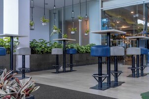 A modern indoor seating area with tables and chairs, potted plants, and hanging lights.