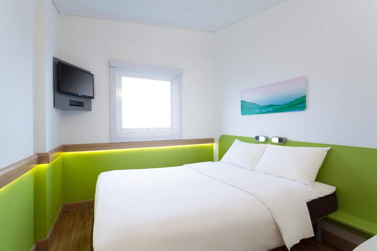 Een hotelkamer met een bed, een aan de muur bevestigde televisie, een raam en een schilderij.