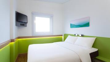 A hotel room with a bed, a TV mounted on the wall, a window, and a painting.