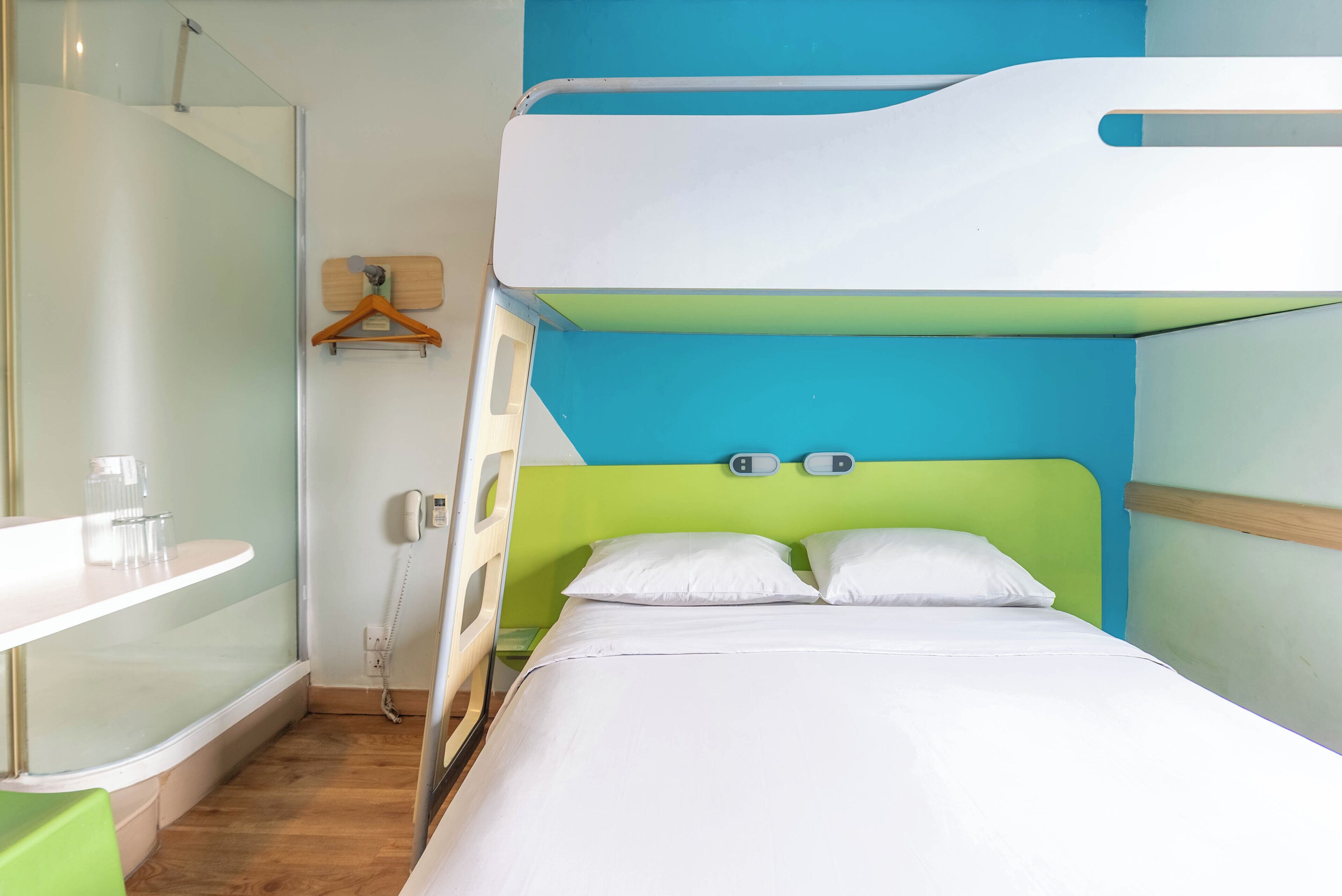 A bunk bed with a green headboard, a bedside table with a glass container, and a wall-mounted phone.