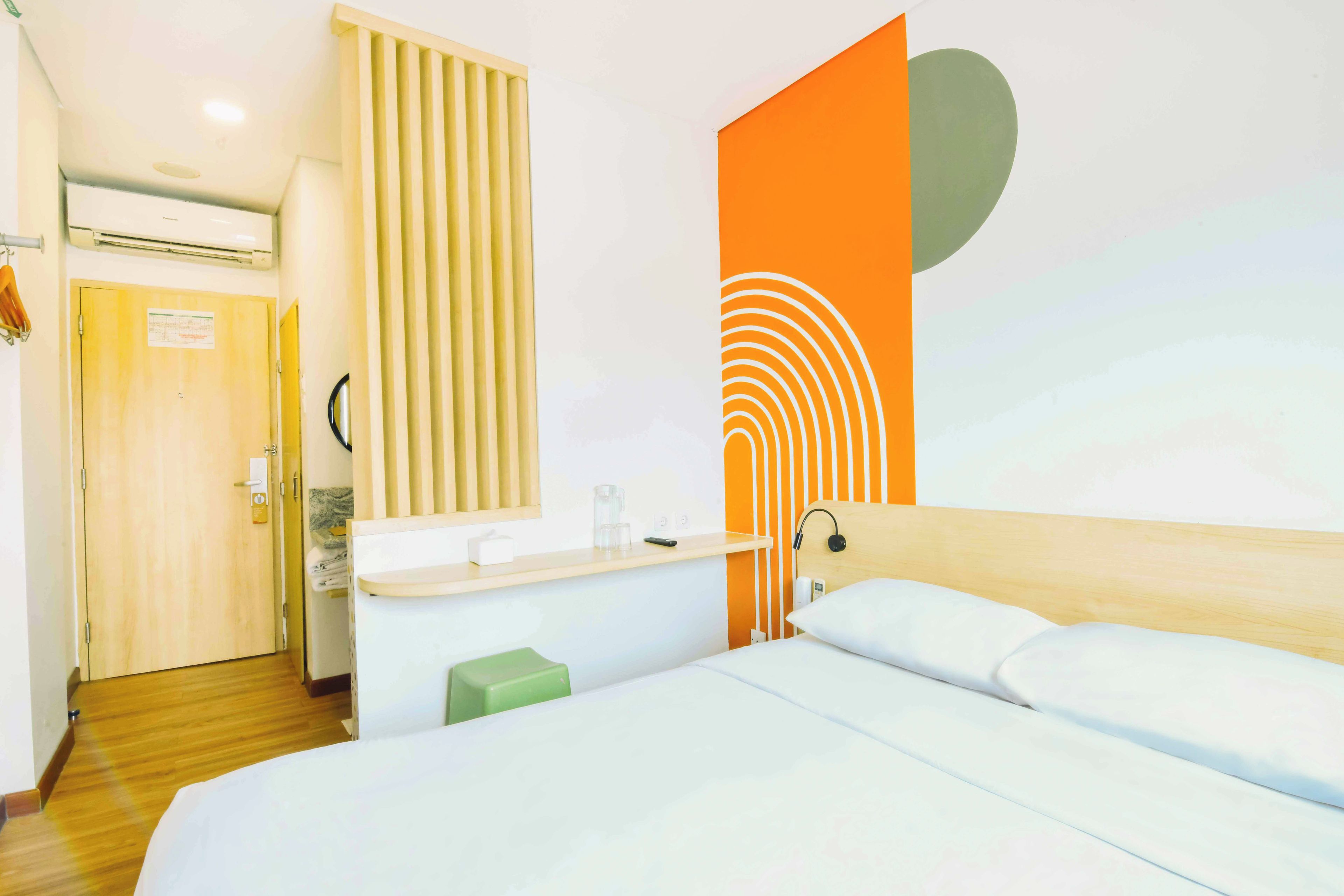 Een hotelkamer met een bed, een houten hoofdbord, een nachtkastje met een lamp en een muur met een geometrisch ontwerp.