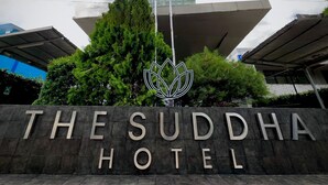 Ein Schild für das Suddha Hotel mit einem modernen Gebäude im Hintergrund.