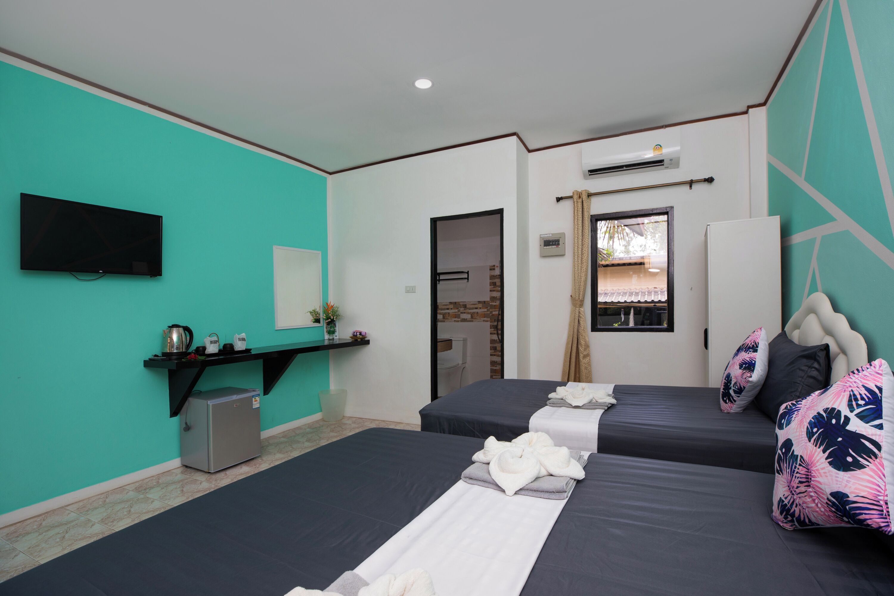 A hotel room with two beds, a TV, a small fridge, a sink, and a window with curtains.