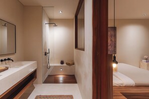 Une salle de bain moderne avec un grand miroir, une douche et une table de chevet avec une lampe.