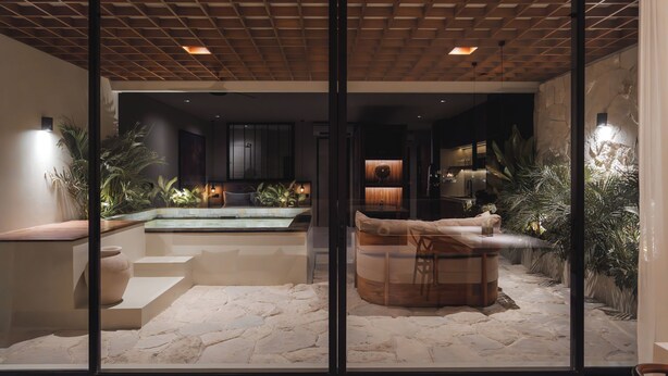 Un espace piscine intérieur moderne, doté d’un sol en pierre, d’un jacuzzi et d’un coin salon avec un banc en bois.