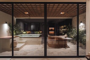 A modern indoor pool area with a stone floor, a hot tub, and a seating area with a wooden bench. - Studio Apartment by Betterplace (Canggu)