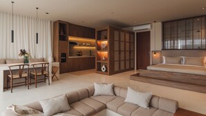 Un salon moderne avec un canapé d’angle, un coin repas avec des chaises en bois et une cuisine dotée de meubles en bois et d’un éclairage suspendu.
