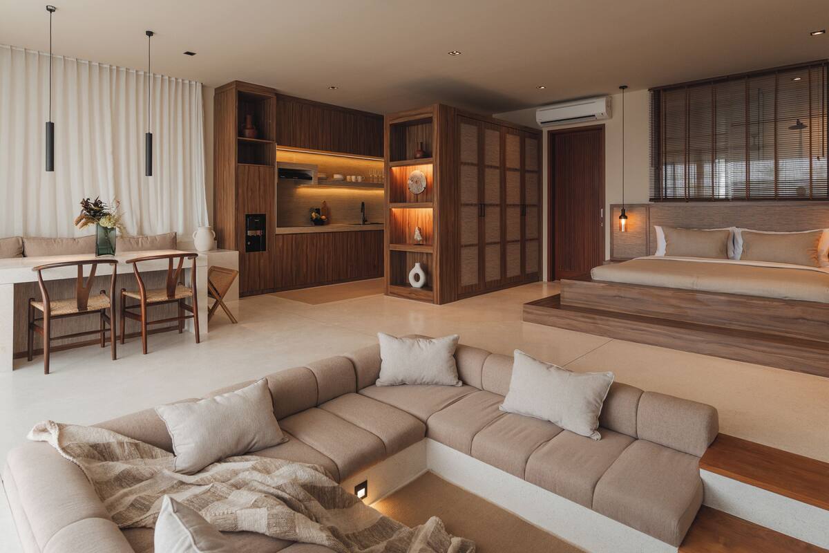 A modern living room with a sectional sofa, a dining area with wooden chairs, and a kitchen with wooden cabinets and pendant lighting.