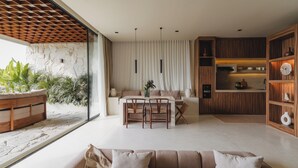 Un salon moderne avec un canapé, une table à manger et des chaises. On y trouve également un coin cuisine avec des meubles en bois et une table à manger. La pièce est dotée d’une grande fenêtre donnant sur l’extérieur, où se trouvent des plantes.