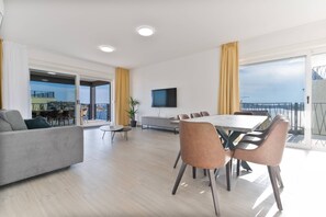 A modern living room with a sofa, dining table, and chairs, a flat-screen TV, and a balcony with a view. - Luxury Living at Horizon Retreat (Marina)