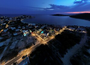 An aerial view of a coastal town at dusk with illuminated buildings, a road, and a body of water. - Luxury Living at Horizon Retreat (Marina)