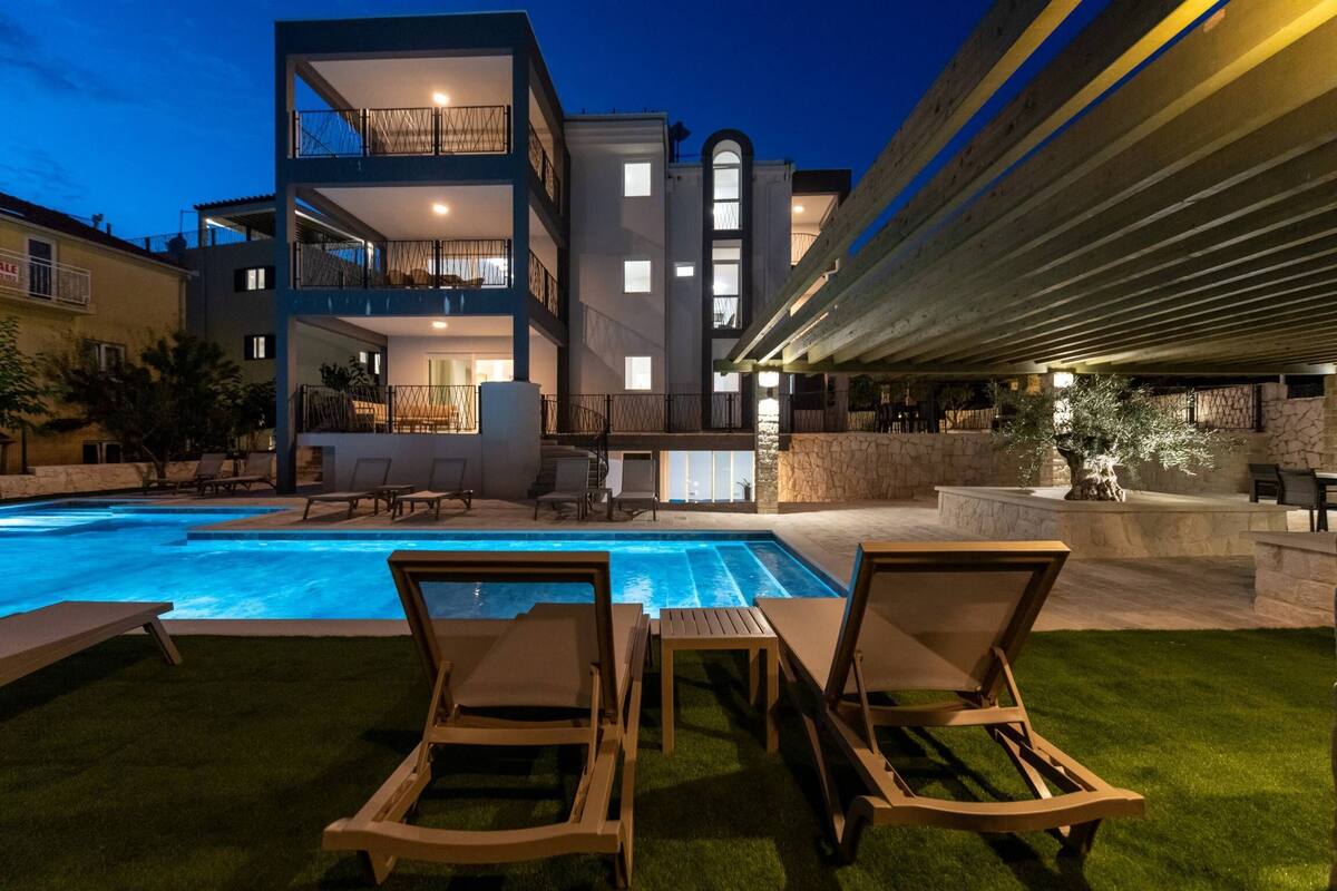 A modern multi-story building with a swimming pool, outdoor seating, and a stone patio.