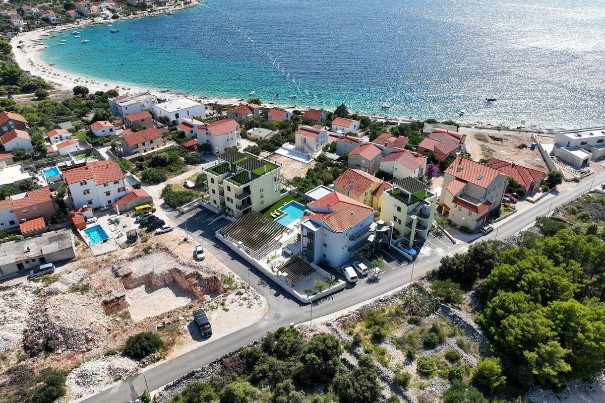 An aerial view of a coastal residential area with houses, a beach, and boats.