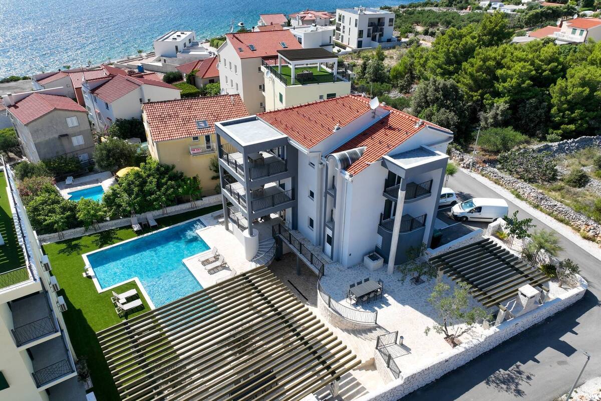 A modern apartment complex with a rooftop pool, multiple balconies, and a view of the sea.