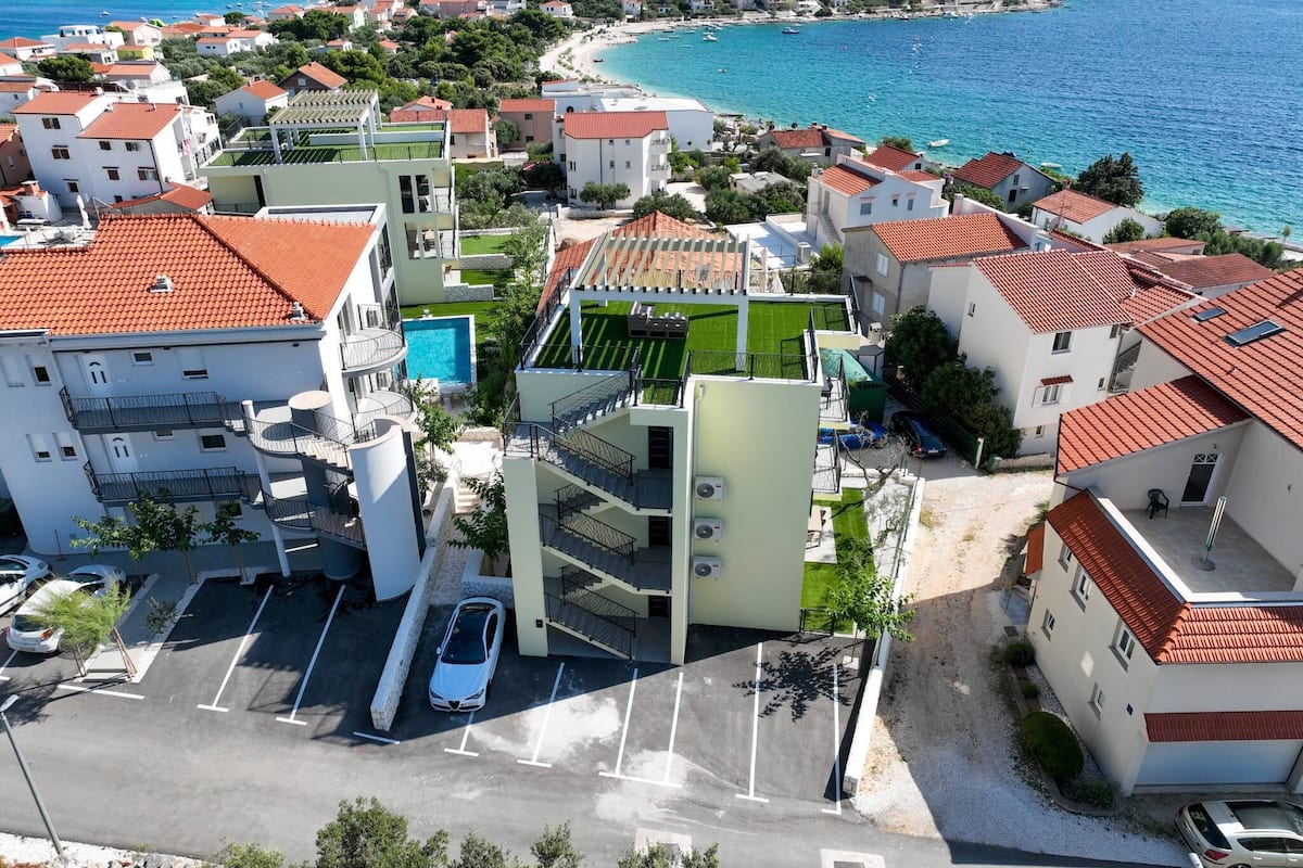 A coastal residential area with modern buildings, a swimming pool, and a view of the sea.