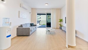 A modern living room with a grey sofa, a small round table, a water dispenser, and a potted plant. - Luxury Living at Horizon Retreat (Marina)