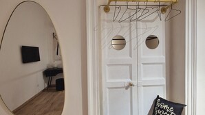 Una habitación con una puerta blanca, un espejo en la pared, un banco negro con un cojín y una percha sobre la puerta.