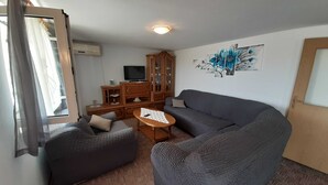 A living room with a grey sofa, a smaller grey armchair, a wooden coffee table, and a cabinet with a television. - Cozy Apartments With Private Balcony Vinisce (Marina)