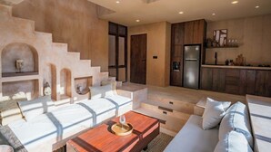 A spacious living area with a staircase leading to a balcony, a kitchen with wooden cabinets, and a seating area with a coffee table. - Villa Alma at Bocoa Villas (Canggu)