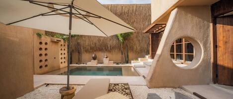 Un área de piscina exterior moderna con techo de paja, sillones de descanso y un diseño arquitectónico único con aberturas circulares.