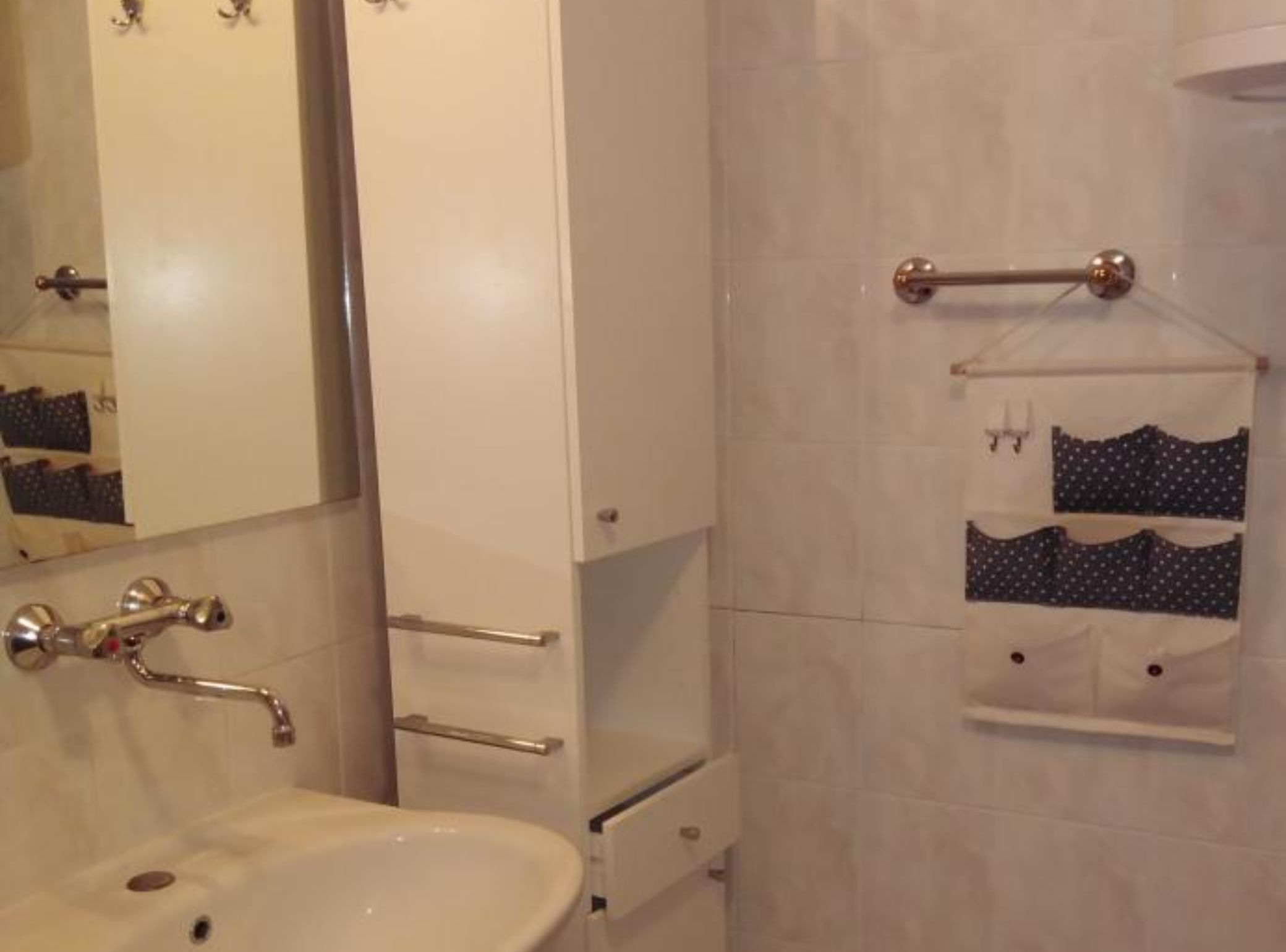 Un baño con lavamanos blanco, espejo, toallero y dispensador de toallas.
