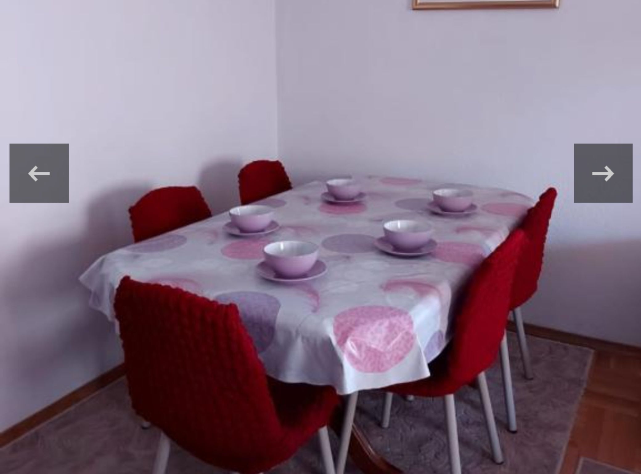 A dining table with a white tablecloth and pink circular patterns, surrounded by red chairs.