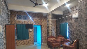 A hotel room with a bed, two armchairs, a wooden wardrobe, a television, and a ceiling fan. - Rani Guest House (Guwahati)